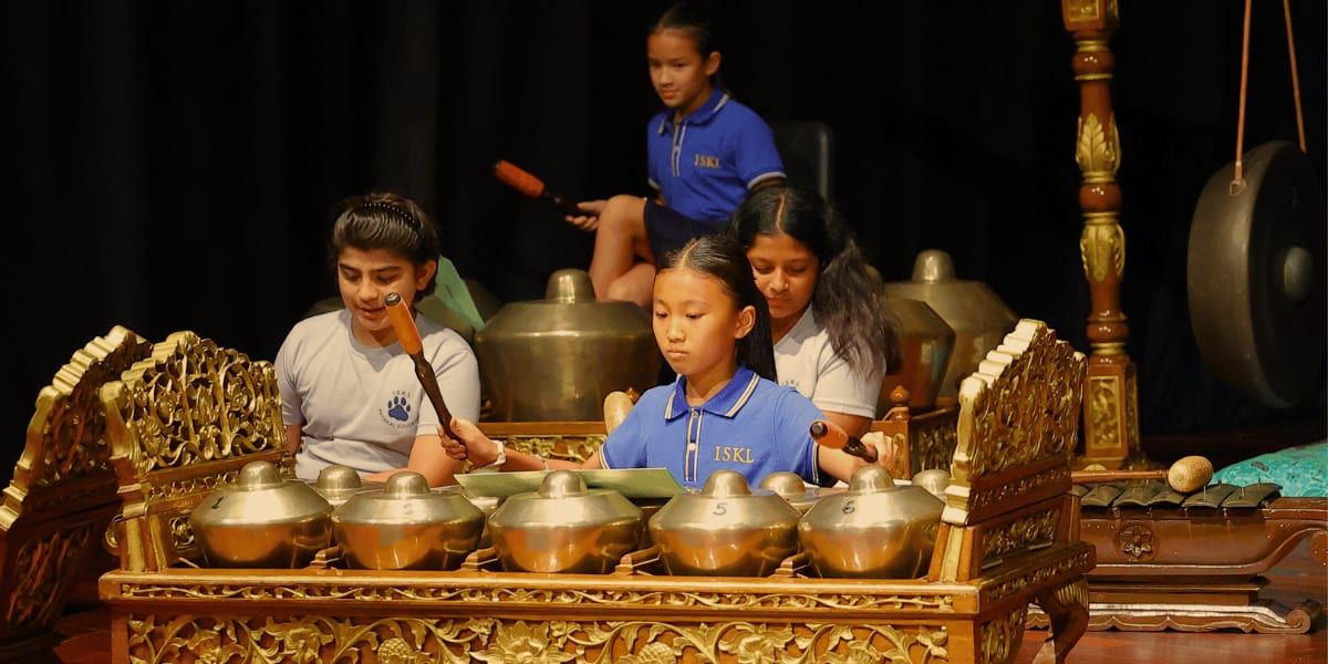 クアラルンプール・インターナショナルスクール: The image depicts a group of students, performing a traditional musical performance on stage, surrounded by ornate golden instruments and decorations.